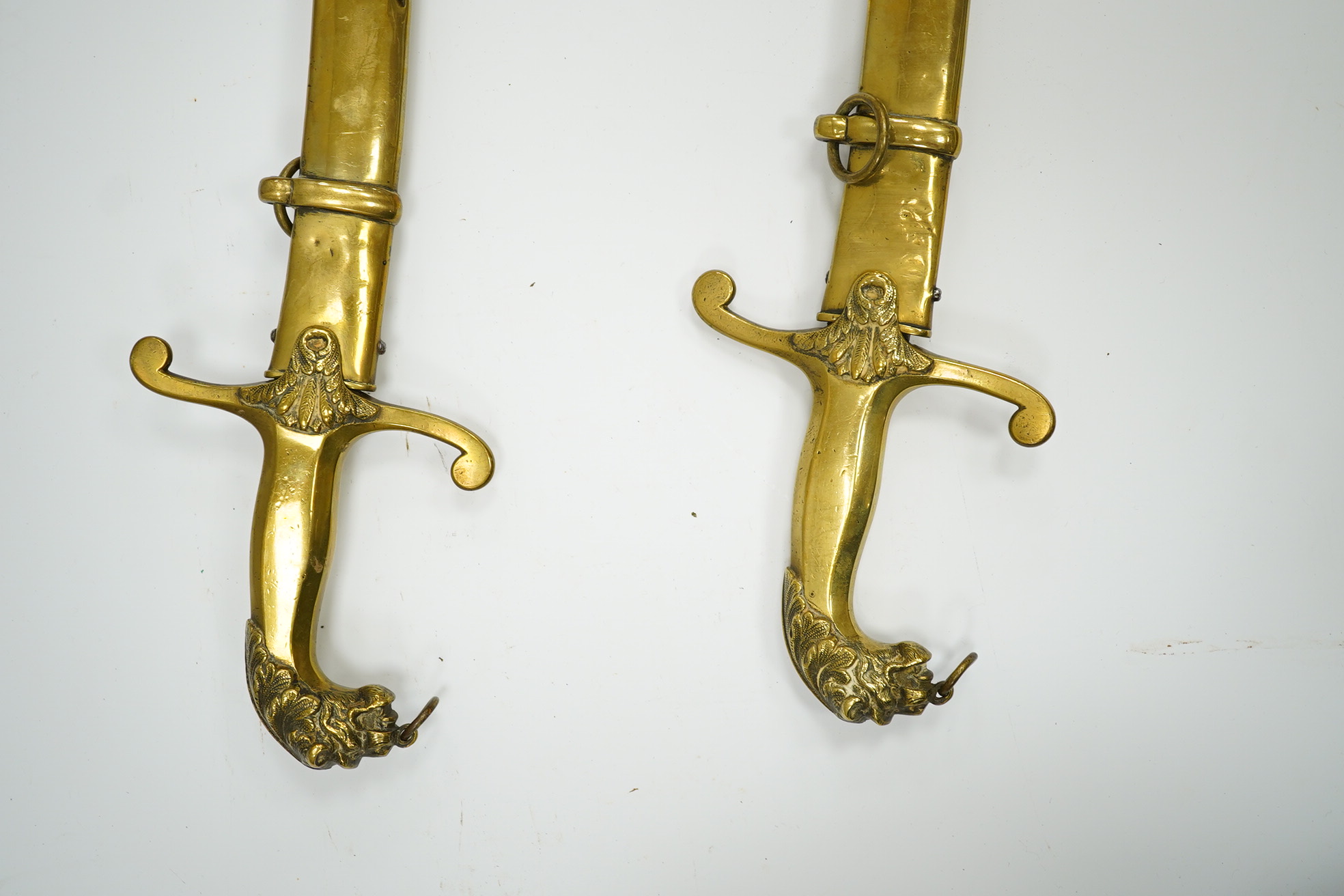 A pair of Victorian bandsman’s swords of Shamshir type, curved single edge blades, cast brass hilts with lions head pommels, in their brass scabbards. Condition - good, some dents to scabbards.